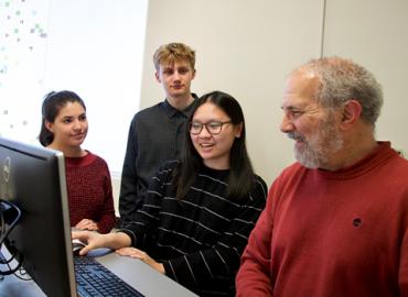 Professor Brad Bass sits with students in front of a computer