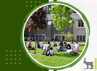 Professional Photo of a group of students sitting on the grass in front of a U of T building. Students are sitting in a circle and listening to a speaker. 